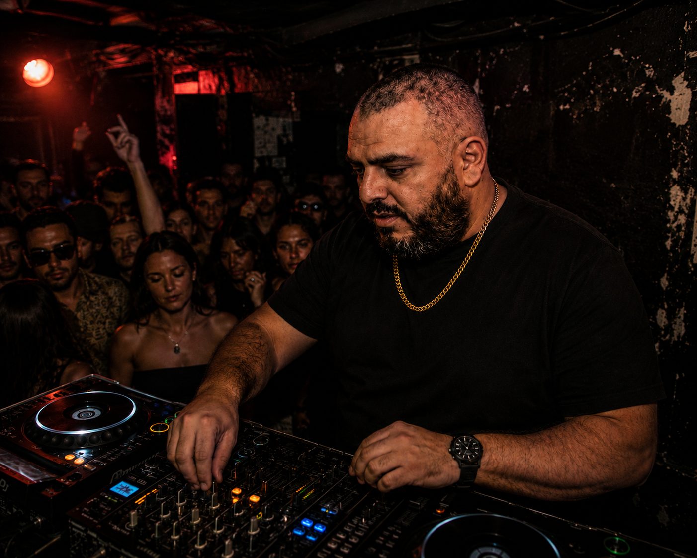 Adam J. Colosimo DJing close to a packed dancefloor crowd in red club lighting